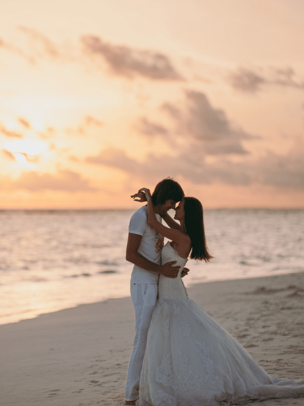 Couple in wedding clothes embraces on the beach during sunset
