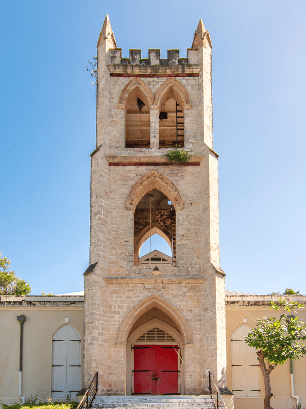 The steeple of a white, Mediterranean-style church with bells and a red door in St. Croix