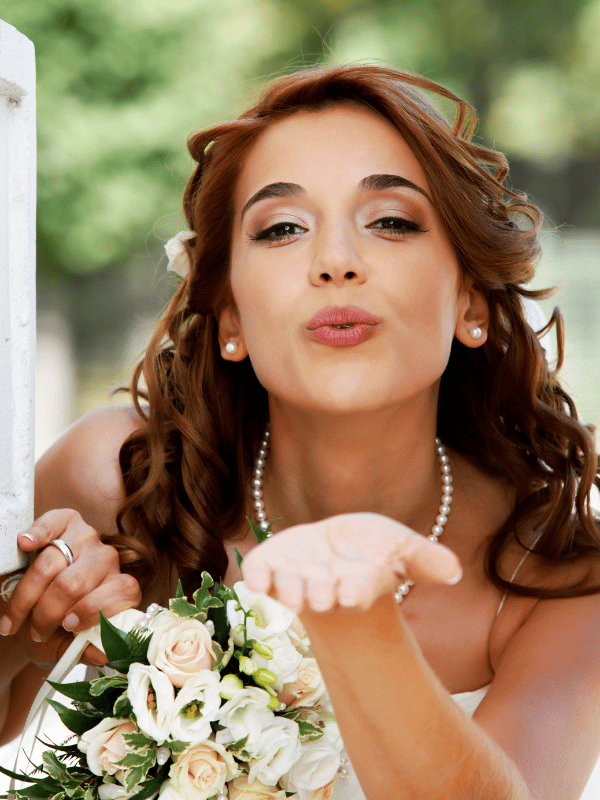 A bride holding a bouquet in one hand blows a kiss at the camera