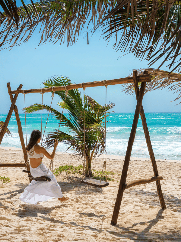 Woman in white swings on a beach in Tulum, Mexico