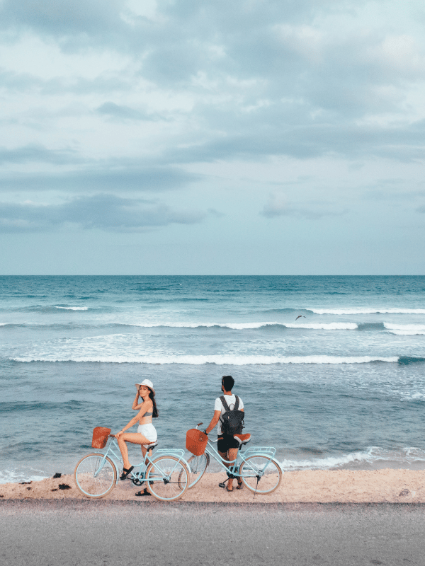 Man and woman ride bicycles along the beach.