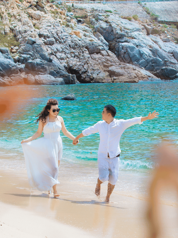 A man and a woman dressed in all white run along a rocky shoreline