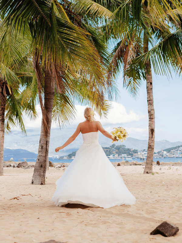 View from behind of a bride running along the beach with palm trees