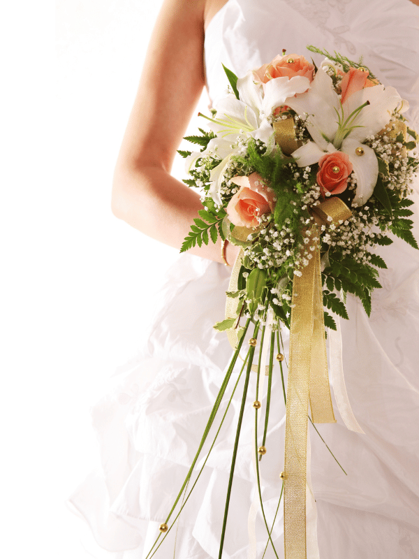 Close-up of bride holding a bouquet with white lilies, pink roses, and greenery