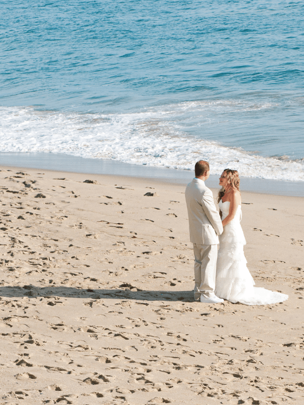 Distance shot of bride and groom facing each other and holding each other's hands on the beach