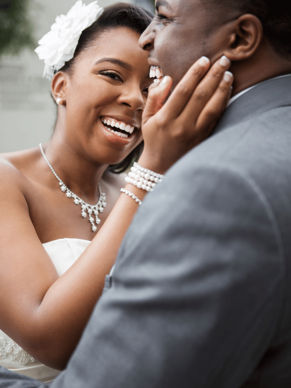 Bride with a flower in her hair caresses her groom's cheek while they both laugh