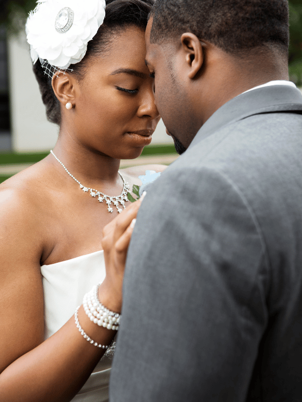 A bride with a flower in her hair touches foreheads with her groom