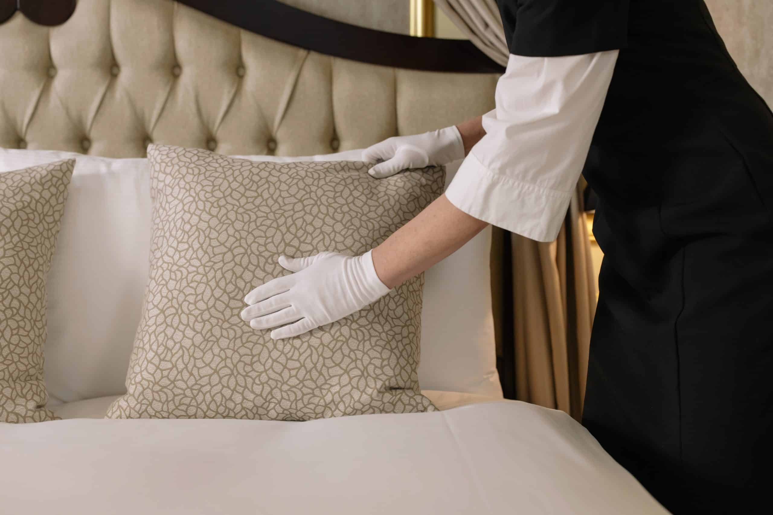 Hotel worker fluffs a pillow.