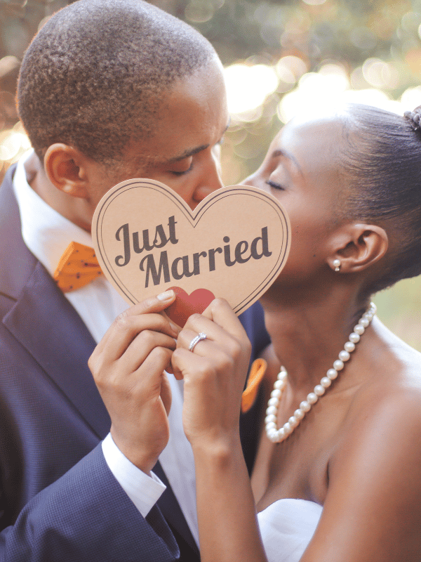 A bride and groom kiss while holding up a sign that says "Just Married"