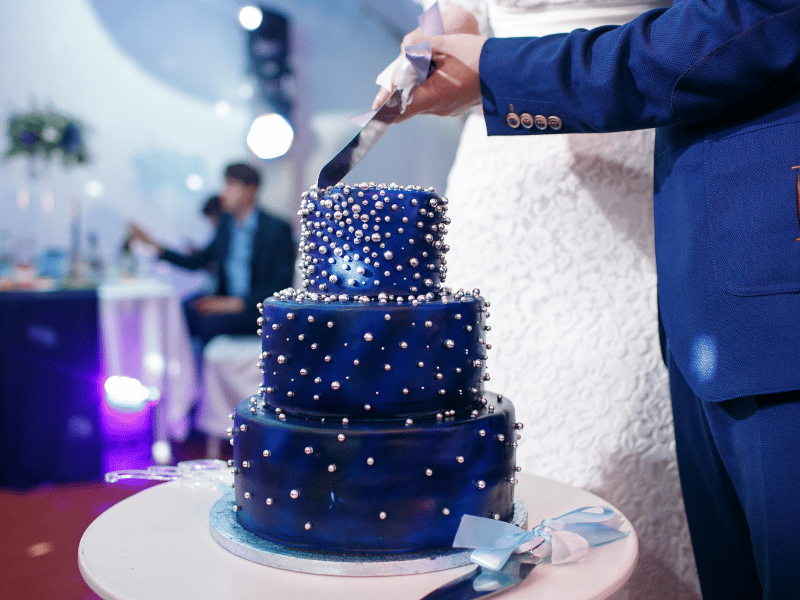 A couple cuts a wedding cake with dark blue galaxy icing and edible pearls.