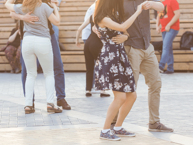 Women in floral dresses and pants dance with men in slacks and casual shirts