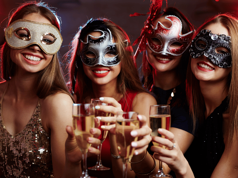 Women in Mardi Gras masks toast champagne