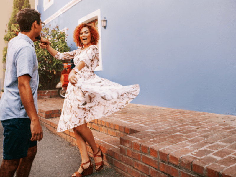 Man in a tee shirt and shorts spins a woman in a floral dress