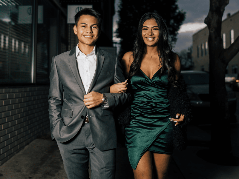 Man in grey suit links arms with woman in satin green dress