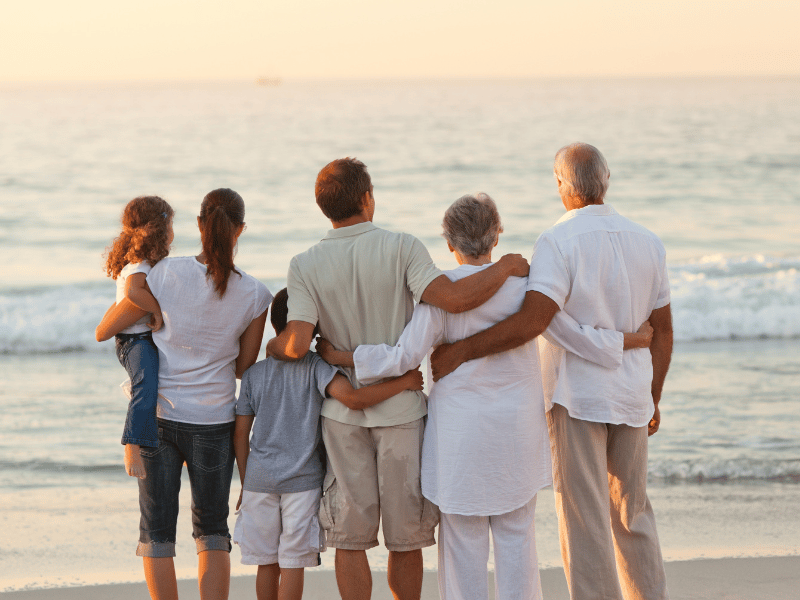 Family stands on the beach together and watches the sunset