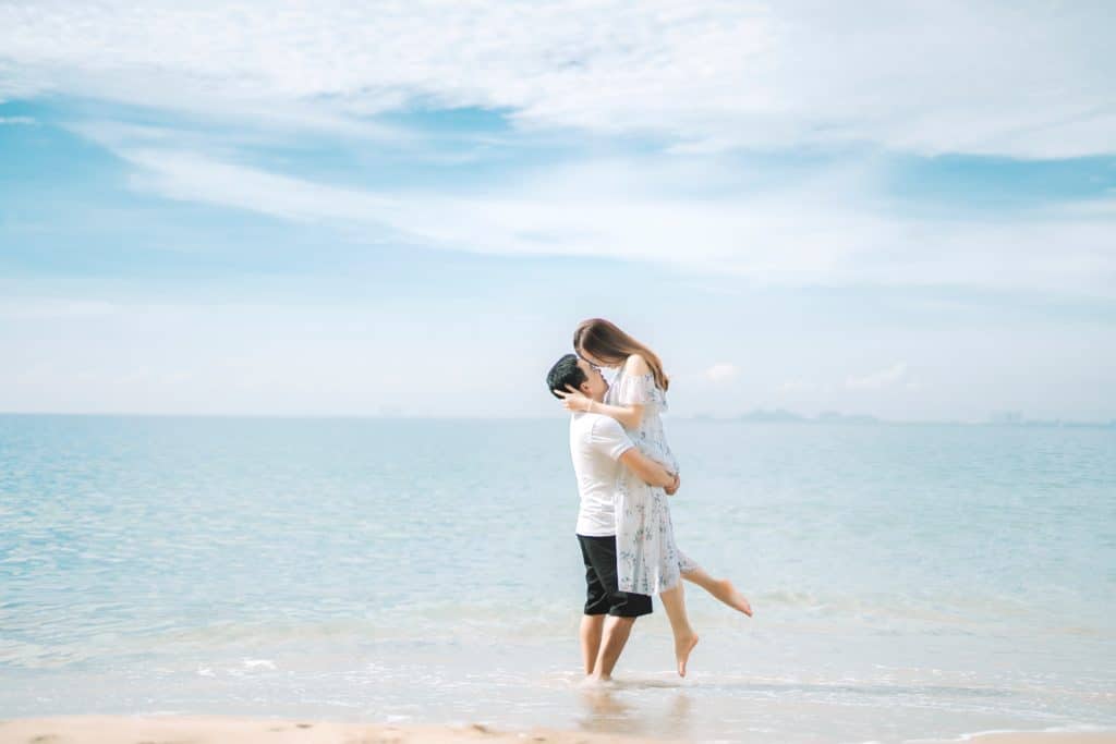 Anonymous couple embracing near ocean on sandy shore.