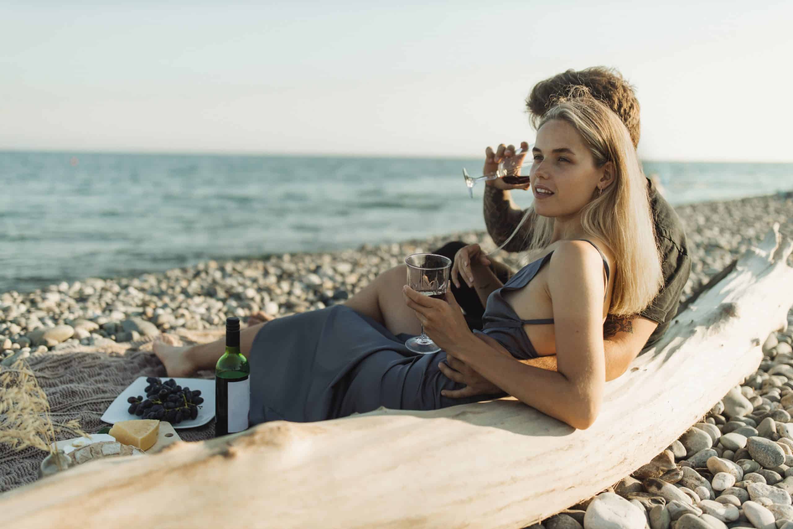 Man and woman on their honeymoon sit on the beach and drink wine together