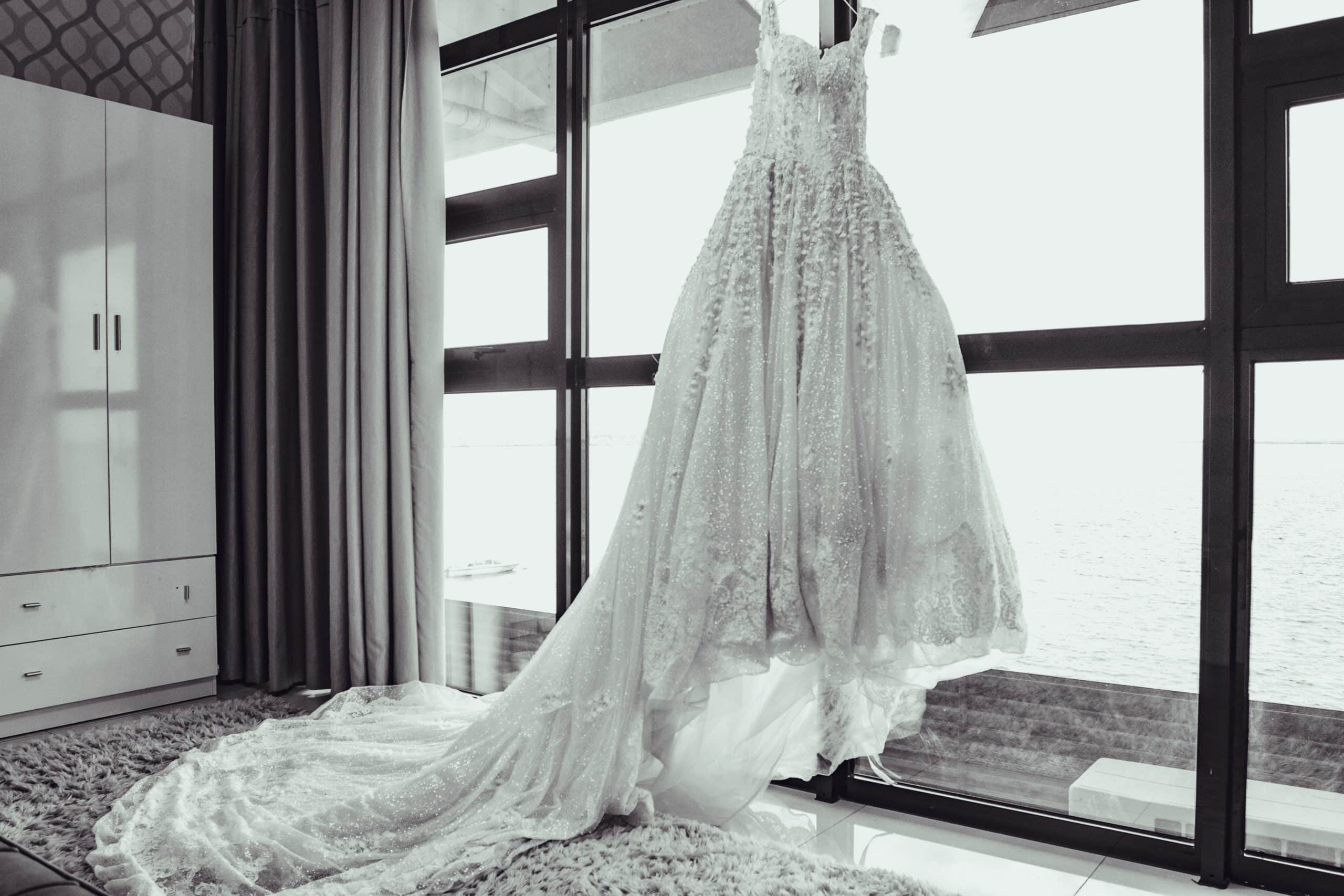 Grayscale photo of a white wedding dress on a window