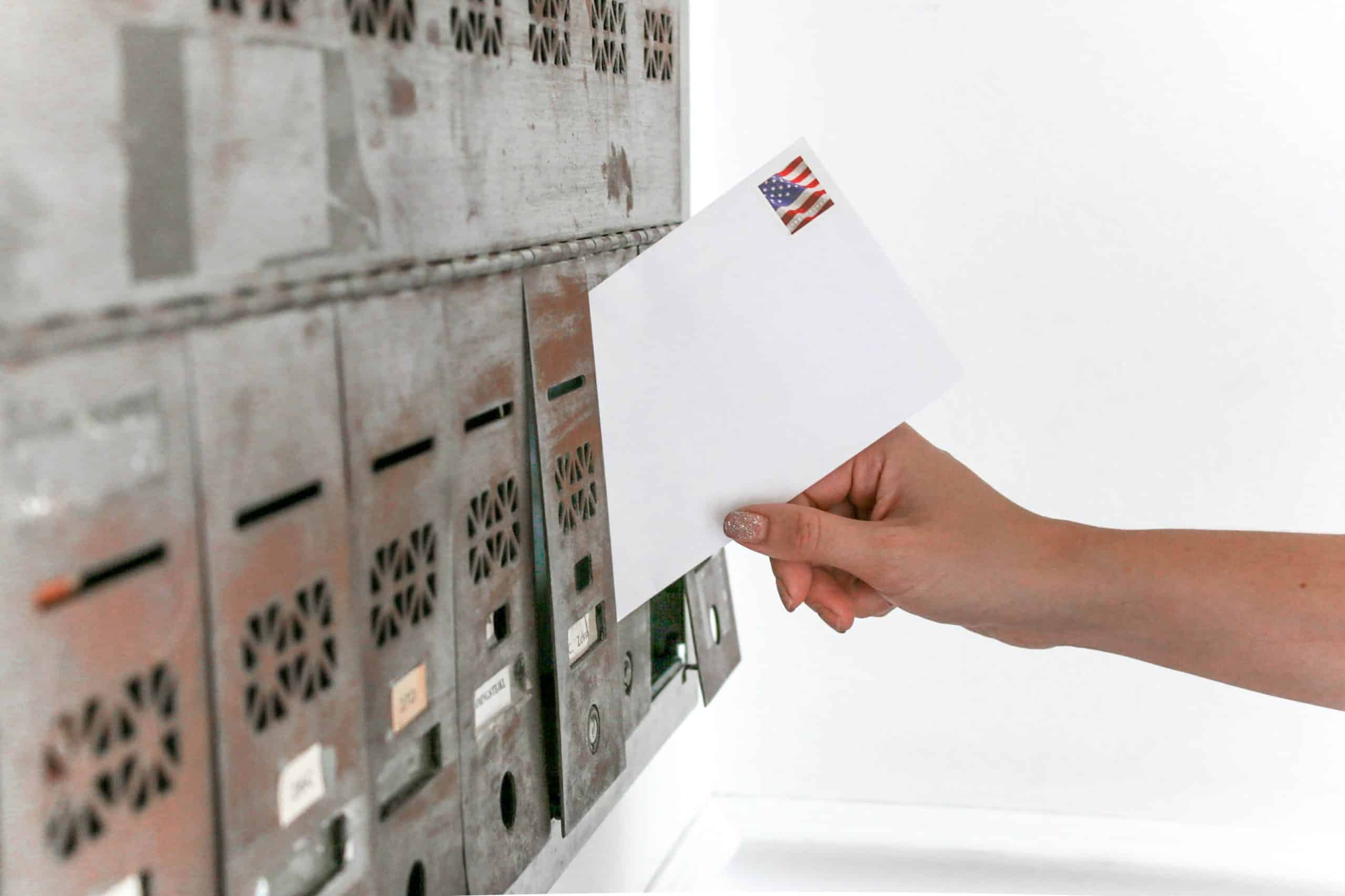 Hand placing white envelope into a mailbox