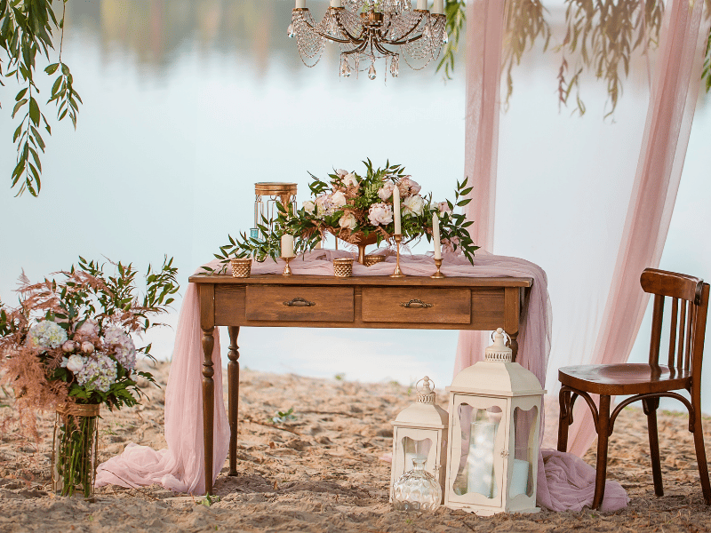A vintage desk and chair on the beach with flowers and lanterns.