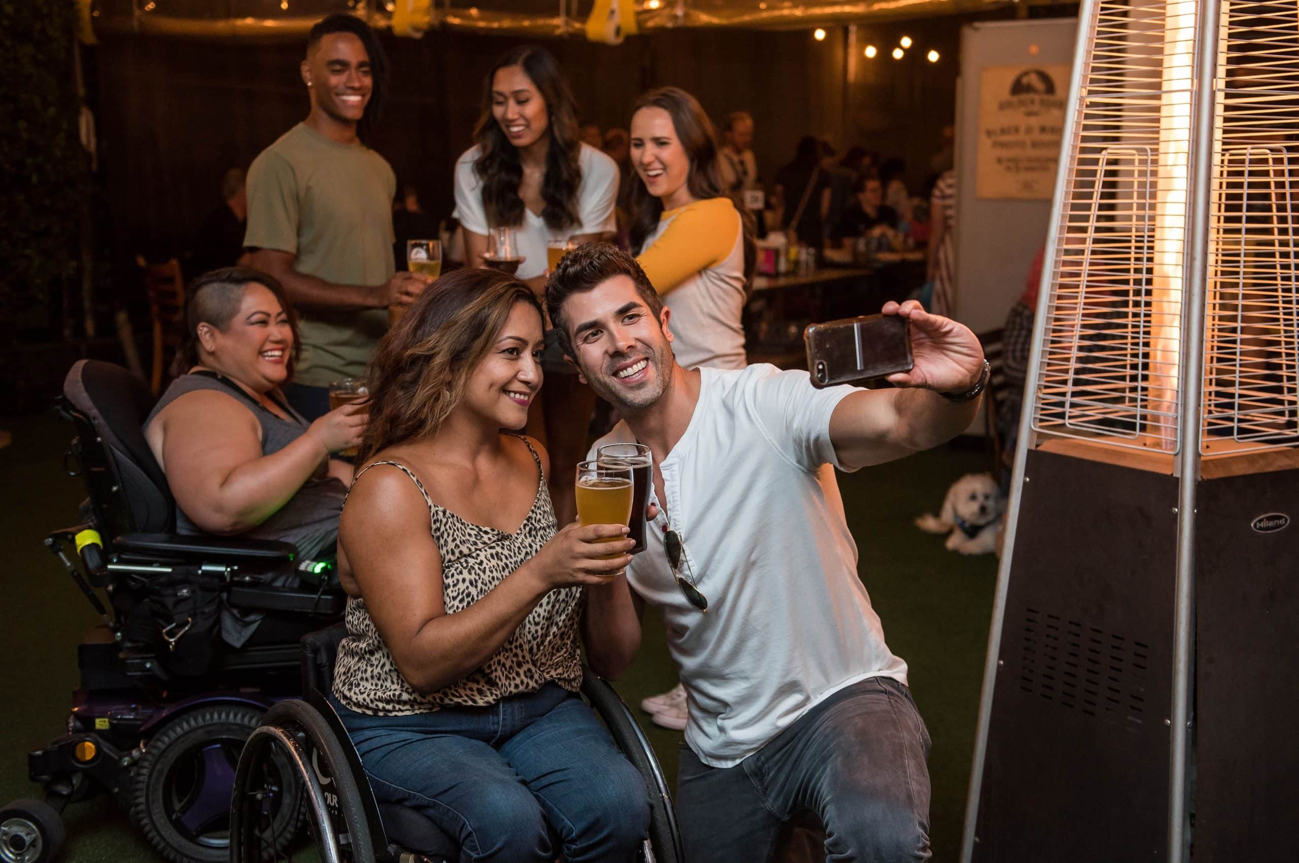 Friend group takes a selfie while holding beers, two of the friends are in wheelchairs