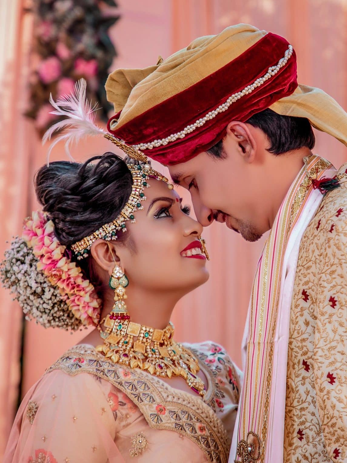 Indian couple in wedding attire touches noses.