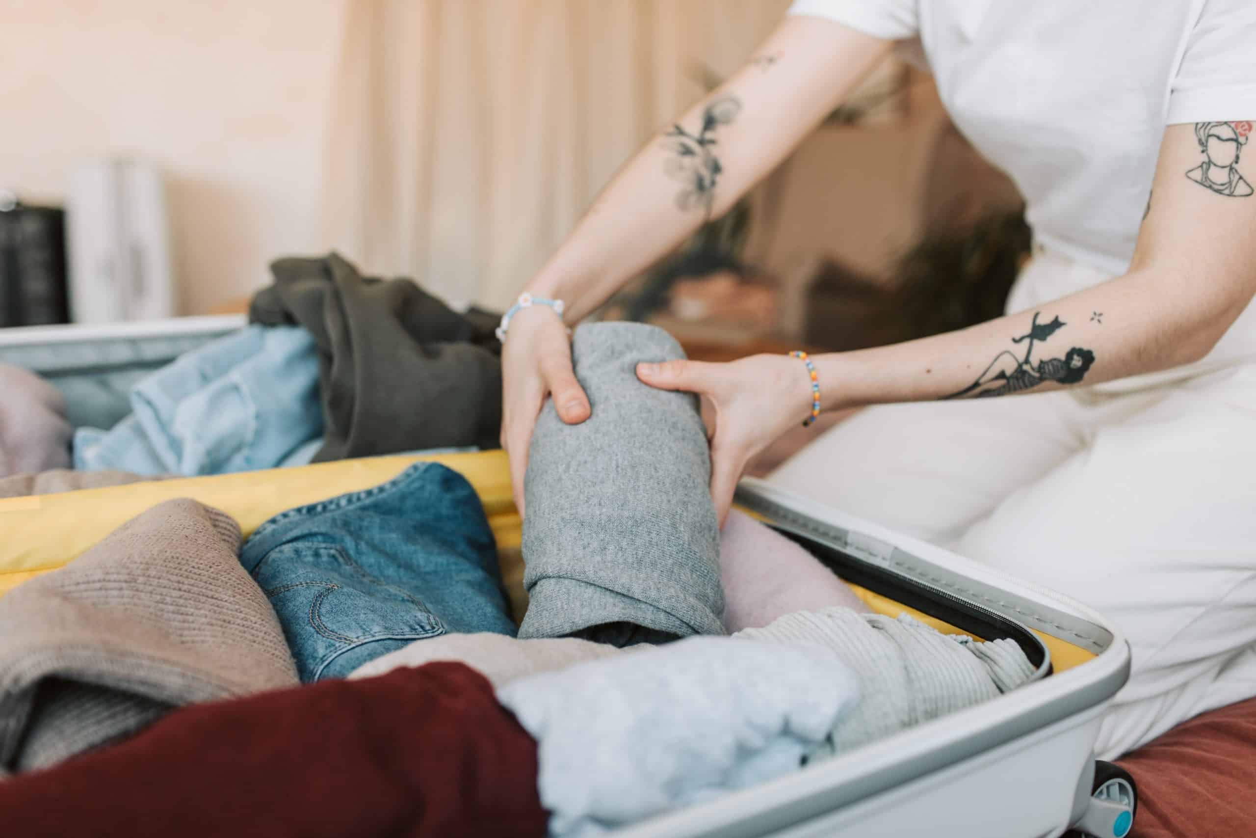 Person with tattoos packs clothes into a suitcase.