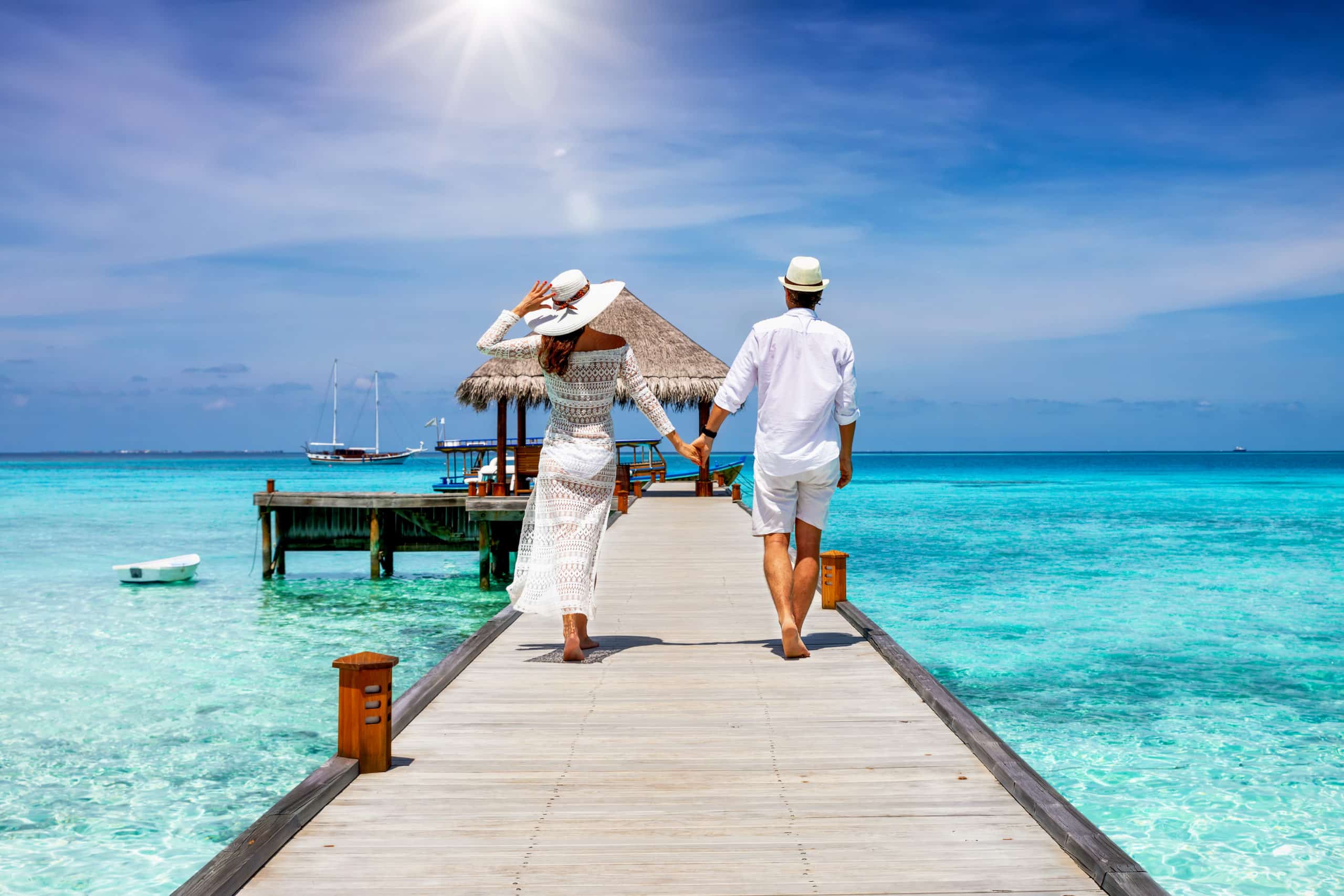 Honeymoon couple walks down a dock by the ocean in the Maldives