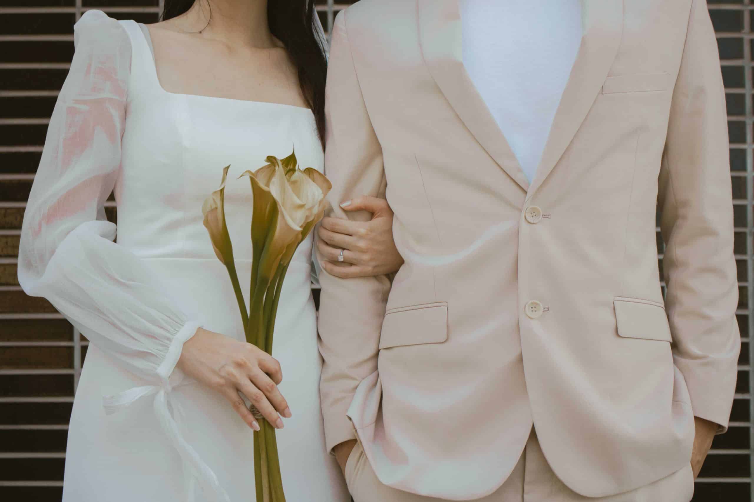 Groom in beige suit and bride with flowing sleeves on her dress holding a bouquet of flowers