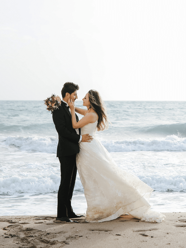Destination wedding couple embracing on beach at ocean's edge