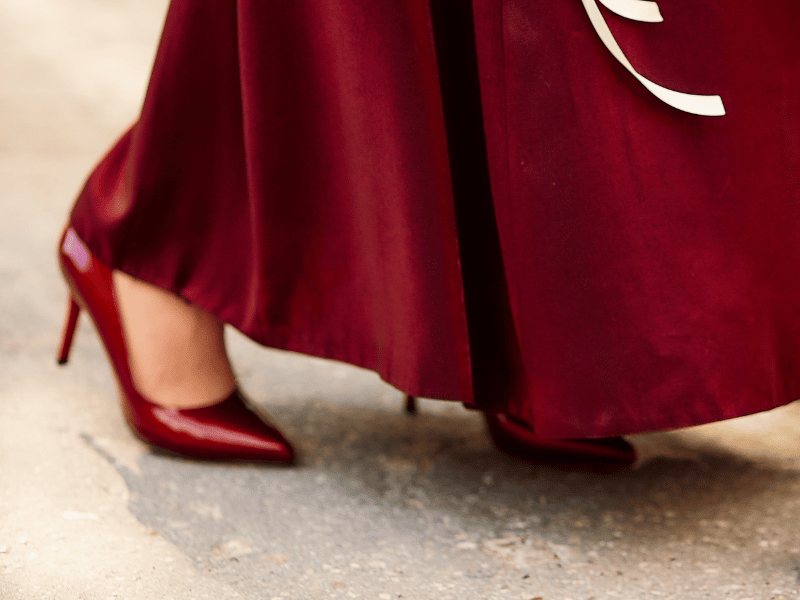 Closeup of the bottom of a bridesmaid's dress in Pantone's Viva Magenta with matching patent leather heels